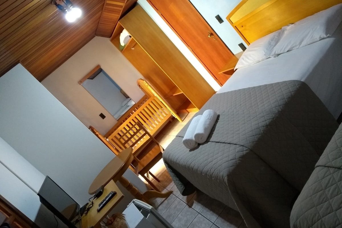 Una habitación de hotel con una cama, techo de madera, una mesita y una silla.