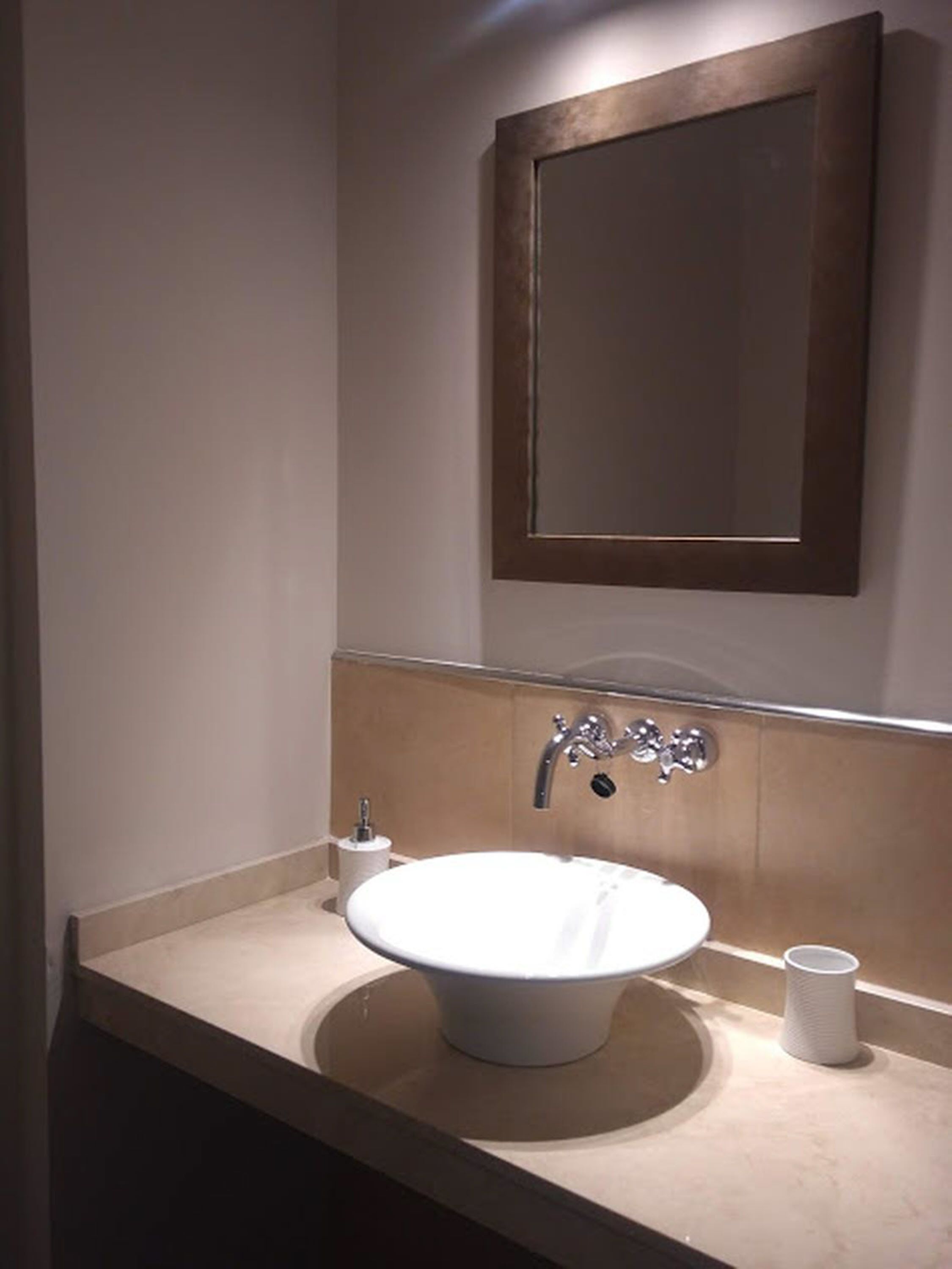A bathroom with a round sink, a mirror, and a towel dispenser.
