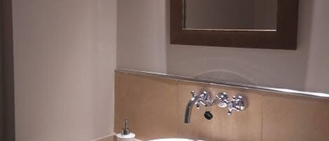 A bathroom with a round sink, a mirror, and a towel dispenser.