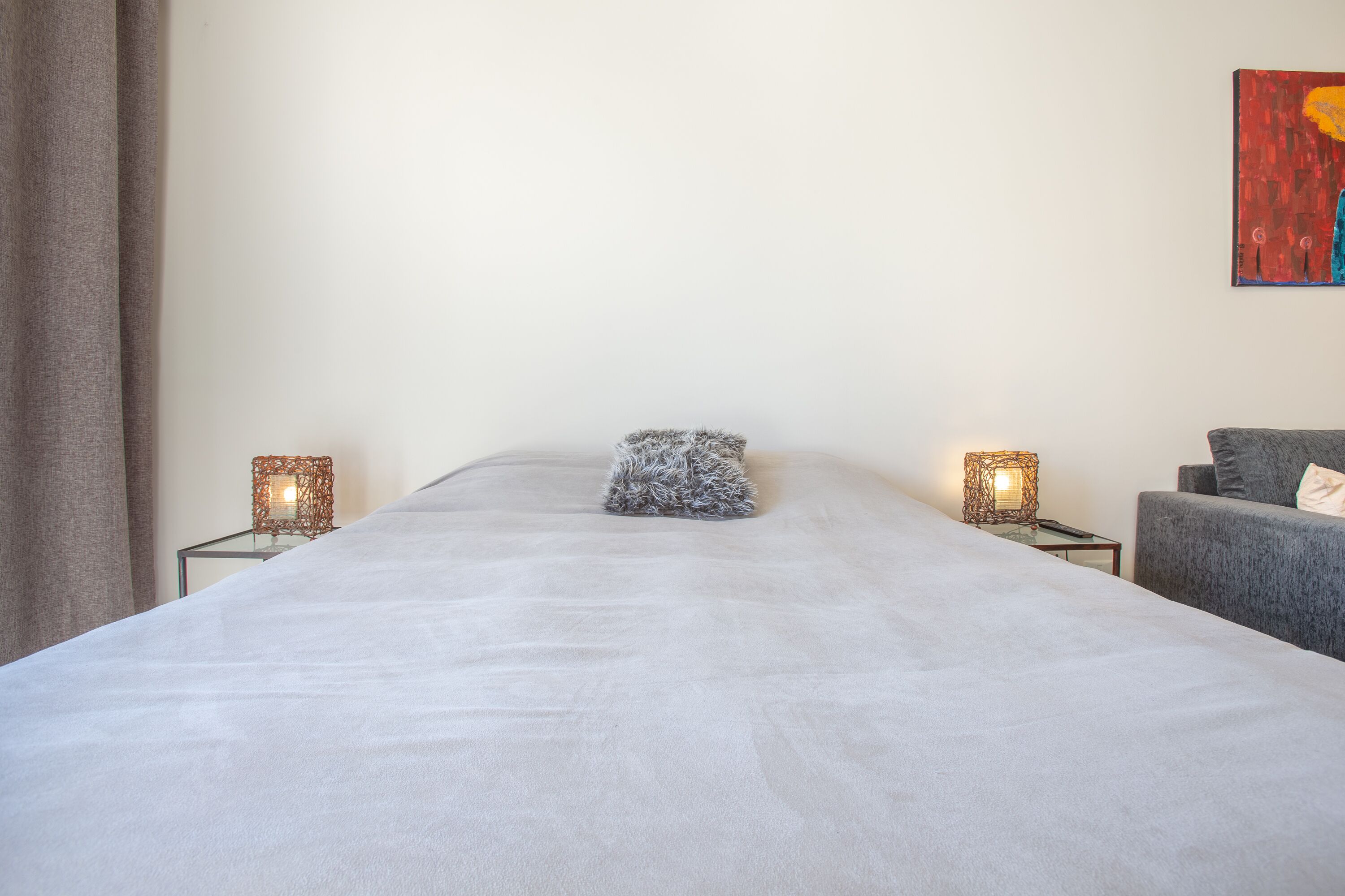 A neatly made bed with a fluffy pillow, two bedside tables with lamps, and a gray armchair.