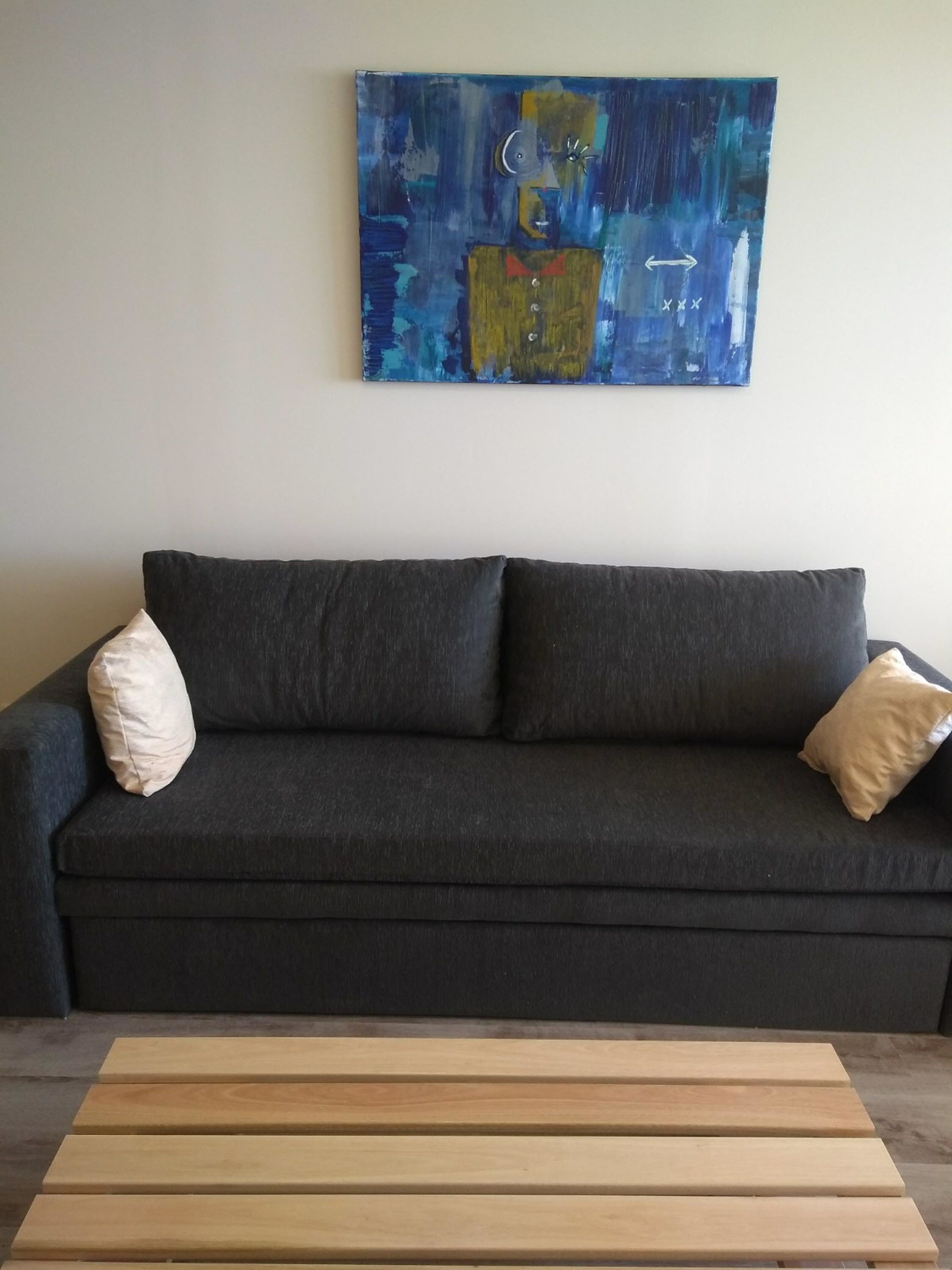 Ein dunkelgraues Sofa mit zwei Kissen, ein Holztisch und ein blaues abstraktes Gemälde an der Wand.
