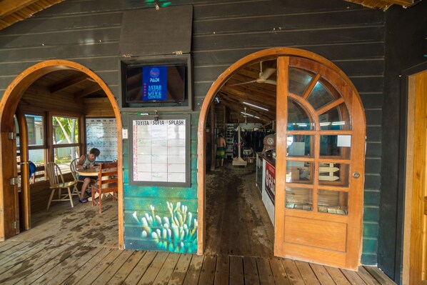 A wooden interior with a wooden table and chairs, a wall calendar, and a TV screen displaying a schedule. - West End Dive Resort (Roatan)