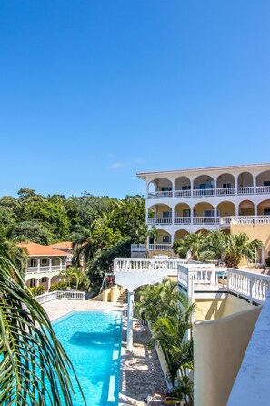 A resort with a swimming pool, a multi-story building with balconies, and lush greenery in the background. - West End Dive Resort (Roatan)