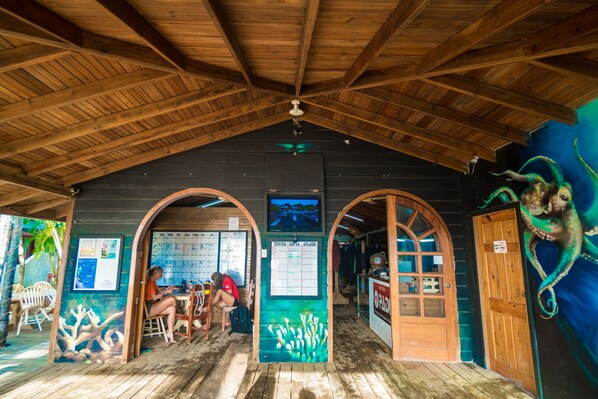 A wooden-roofed building with a wooden table and chairs, a calendar, and a door with a sign. - West End Dive Resort (Roatan)
