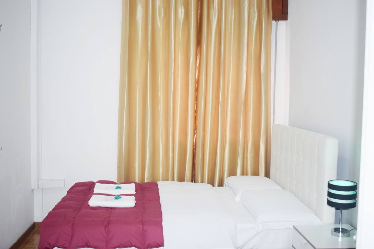 A neatly made bed with a white and maroon bedspread, a white pillow, and a bedside lamp.