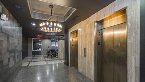 A modern hallway with polished granite floors, a central chandelier, and two elevators. - The Nashville Reserve (Nashville)