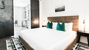 A modern bedroom with a large bed, wooden headboard, and a view of a bathroom and kitchen area. - The Nashville Reserve (Nashville)