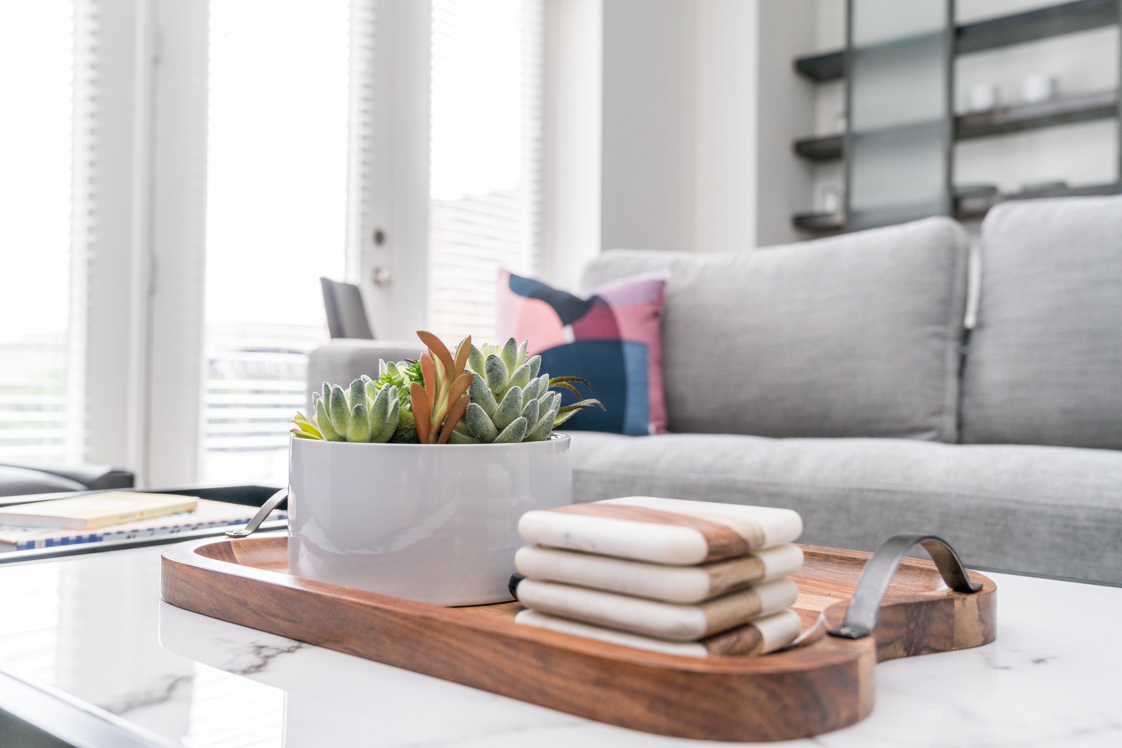 Een moderne woonkamer met een witte salontafel, een pot met een vetplant en een houten dienblad met opgestapelde handdoeken.