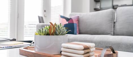 Een moderne woonkamer met een witte salontafel, een pot met een vetplant en een houten dienblad met opgestapelde handdoeken.