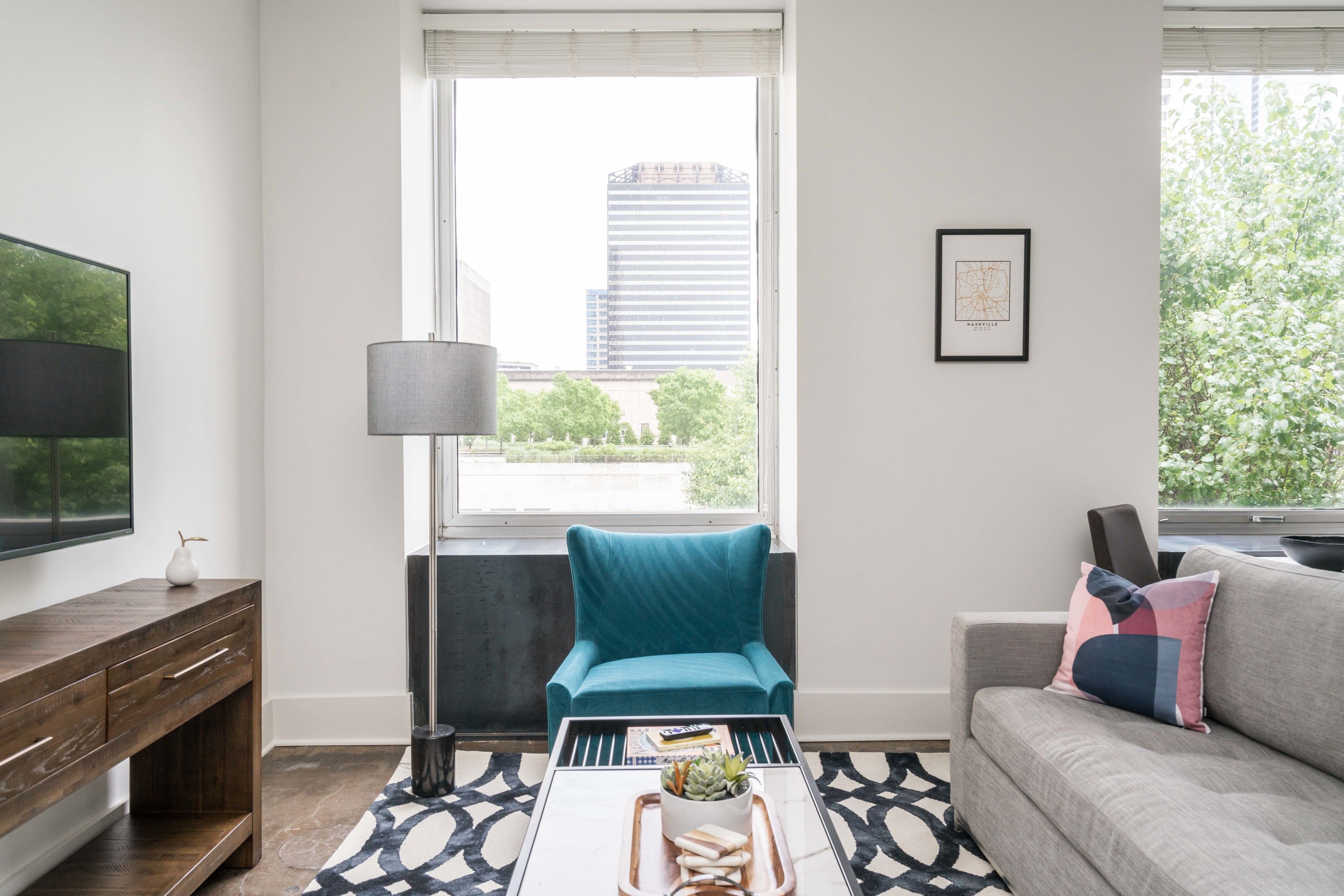 A modern living room with a teal armchair, a grey sofa, and a coffee table with a magazine and a plant.