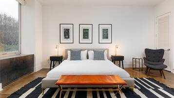 A modern bedroom with a large bed, bedside tables, a bench, a chair, and framed artwork on the wall.