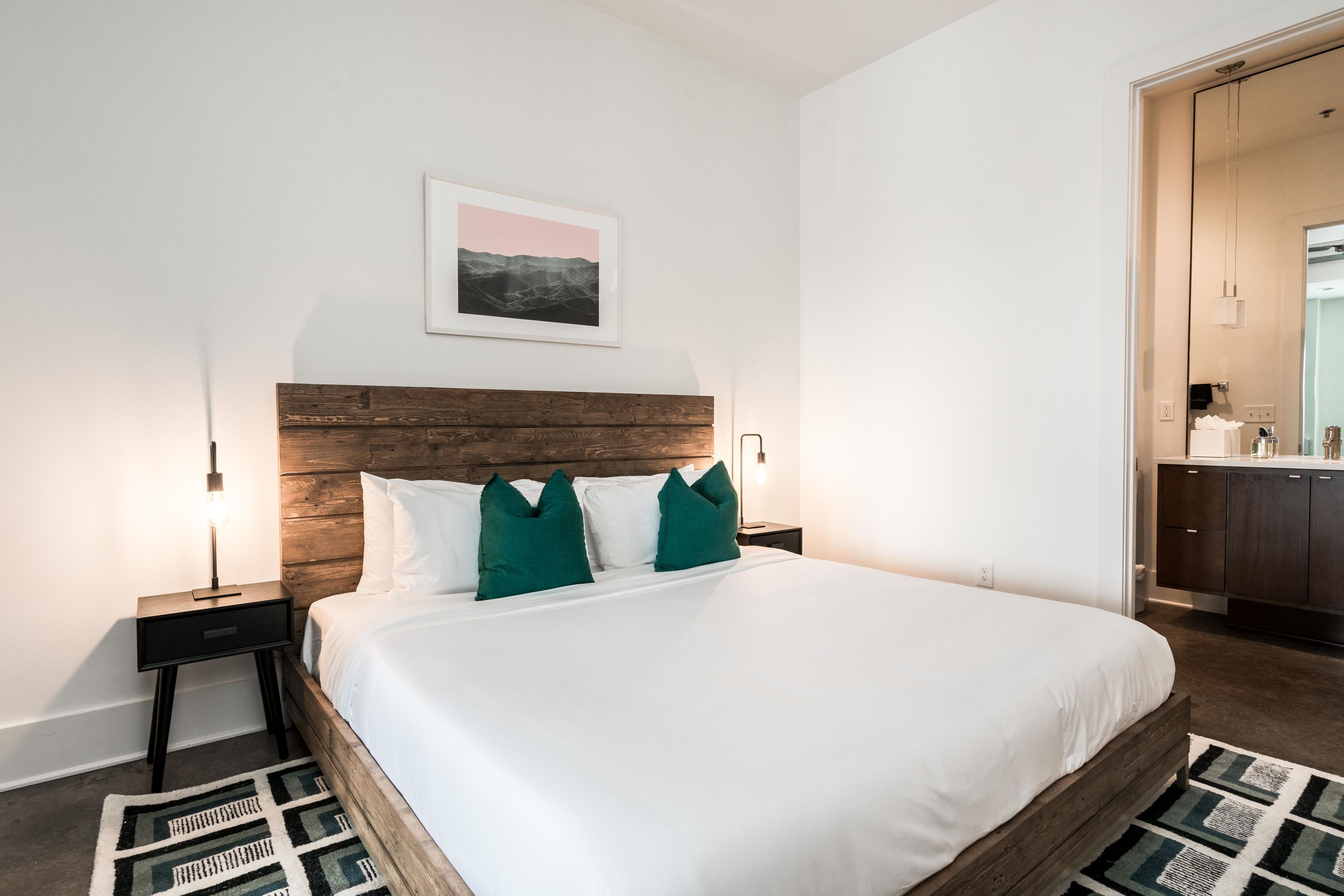 Ein Schlafzimmer mit einem hölzernen Kopfteil, weißer Bettwäsche und einem geometrischen Teppich.