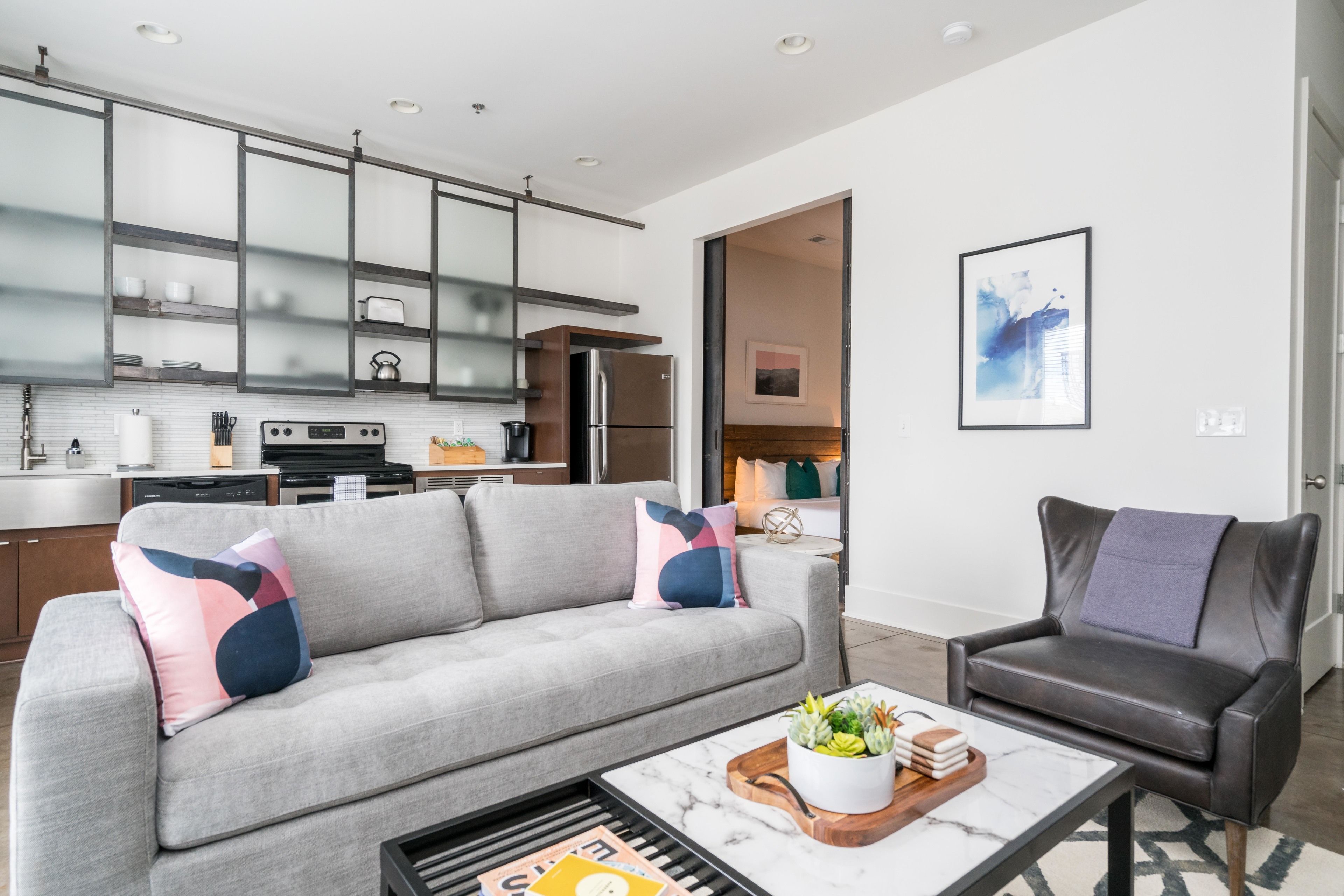 A modern living room with a grey sofa, a coffee table with a magazine, and a black leather chair.