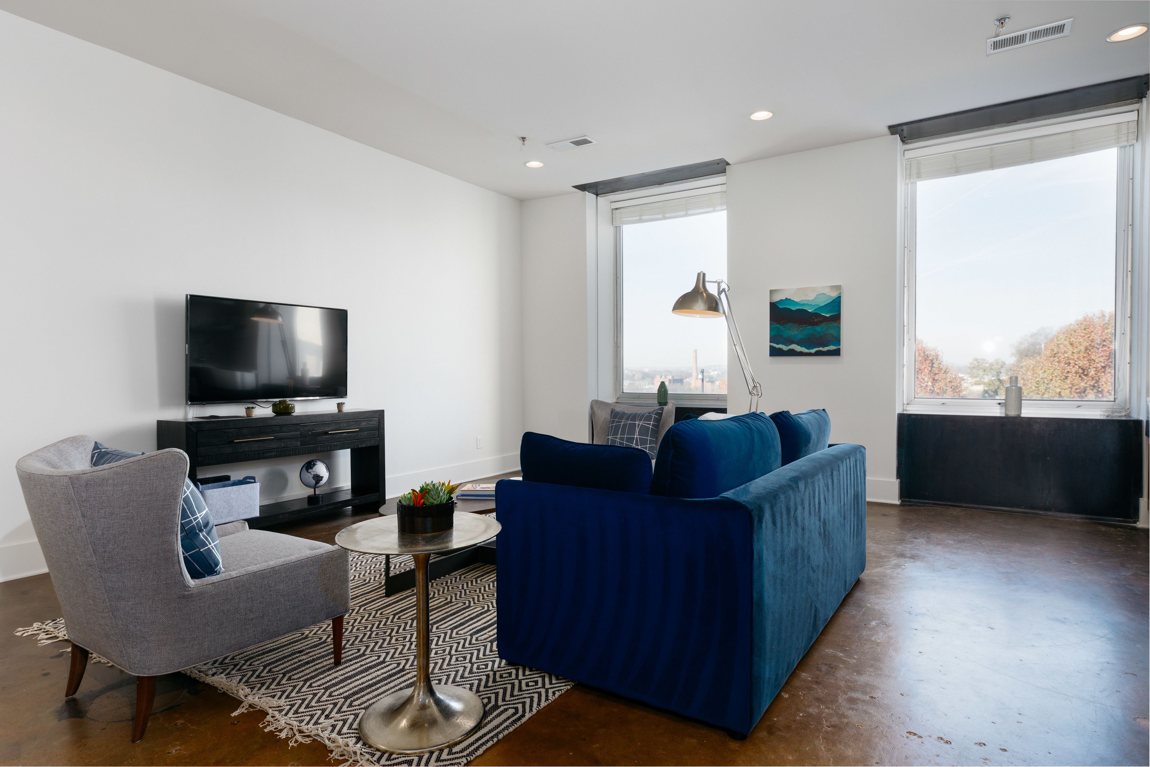 Un salon moderne avec un téléviseur à écran plat, un canapé bleu, un fauteuil gris et un tapis à motifs.
