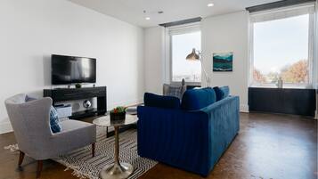 A modern living room with a flat-screen TV, a blue sofa, a grey armchair, and a patterned rug.