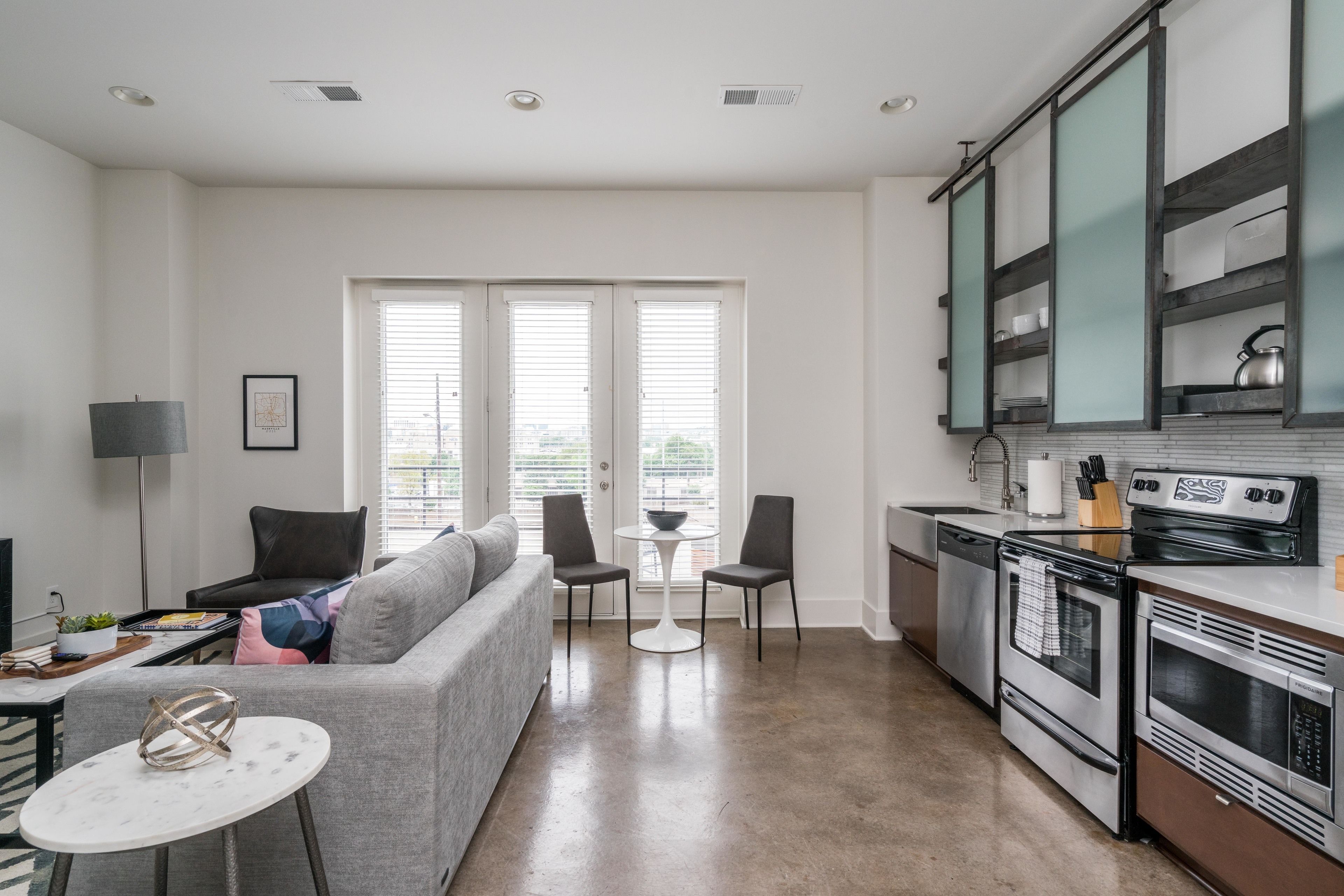 Een moderne keuken met roestvrijstalen apparatuur, een grijze bank en een eethoek met twee stoelen en een kleine tafel.