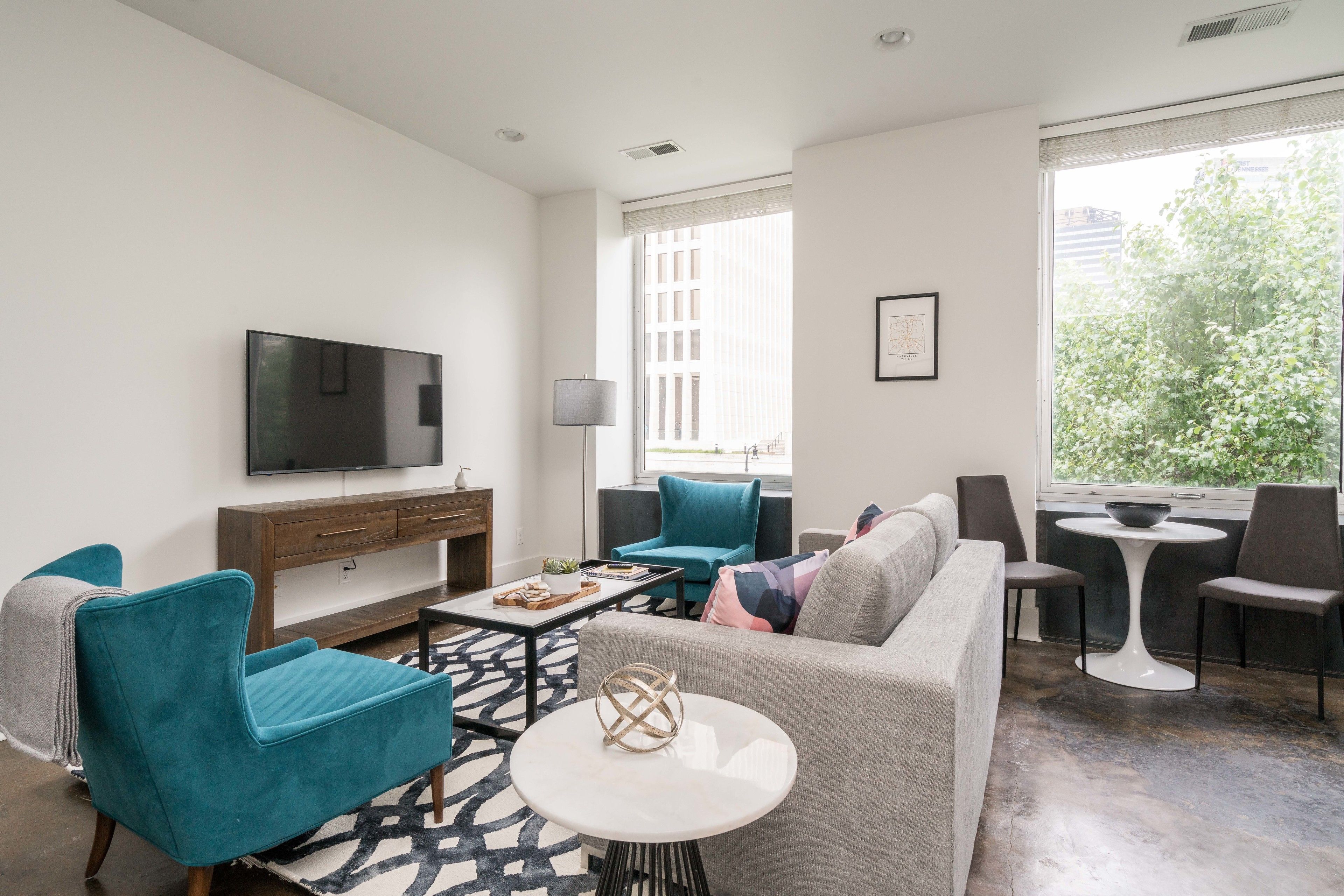 A modern living room with a sofa, teal armchairs, a coffee table, and a TV.