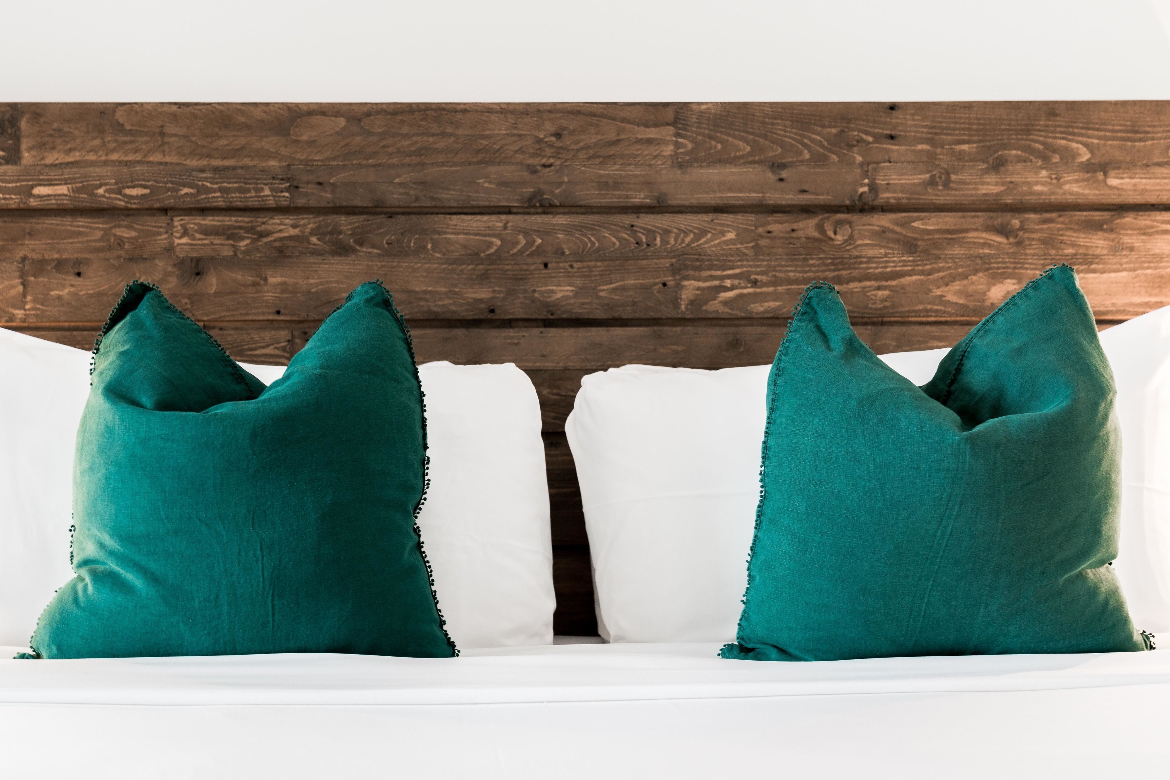 A white sofa with two teal pillows and a wooden headboard.