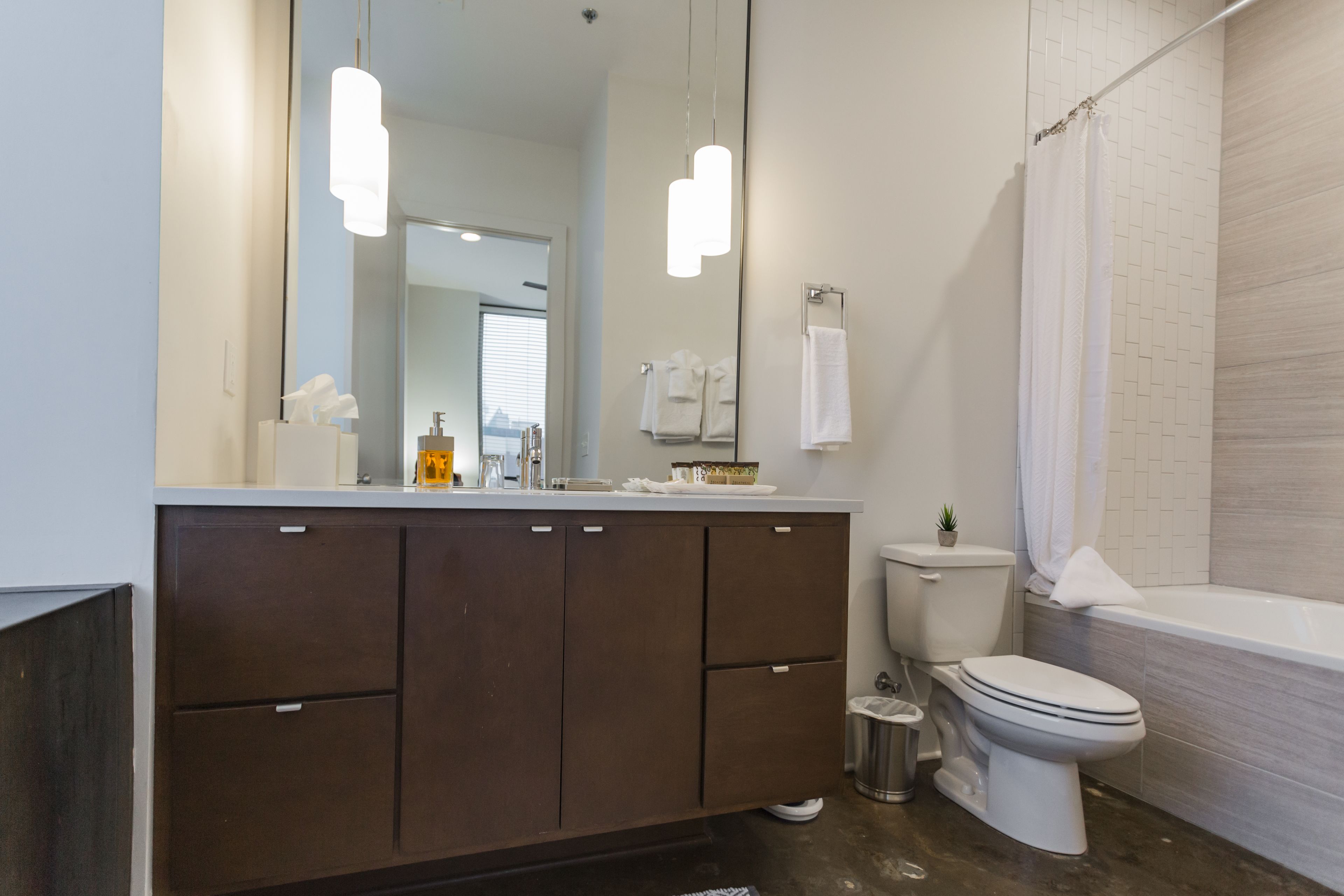 A modern bathroom with a large mirror, a toilet, a bathtub, and a vanity with cabinets.