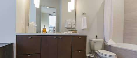 A modern bathroom with a large mirror, a toilet, a bathtub, and a vanity with cabinets.