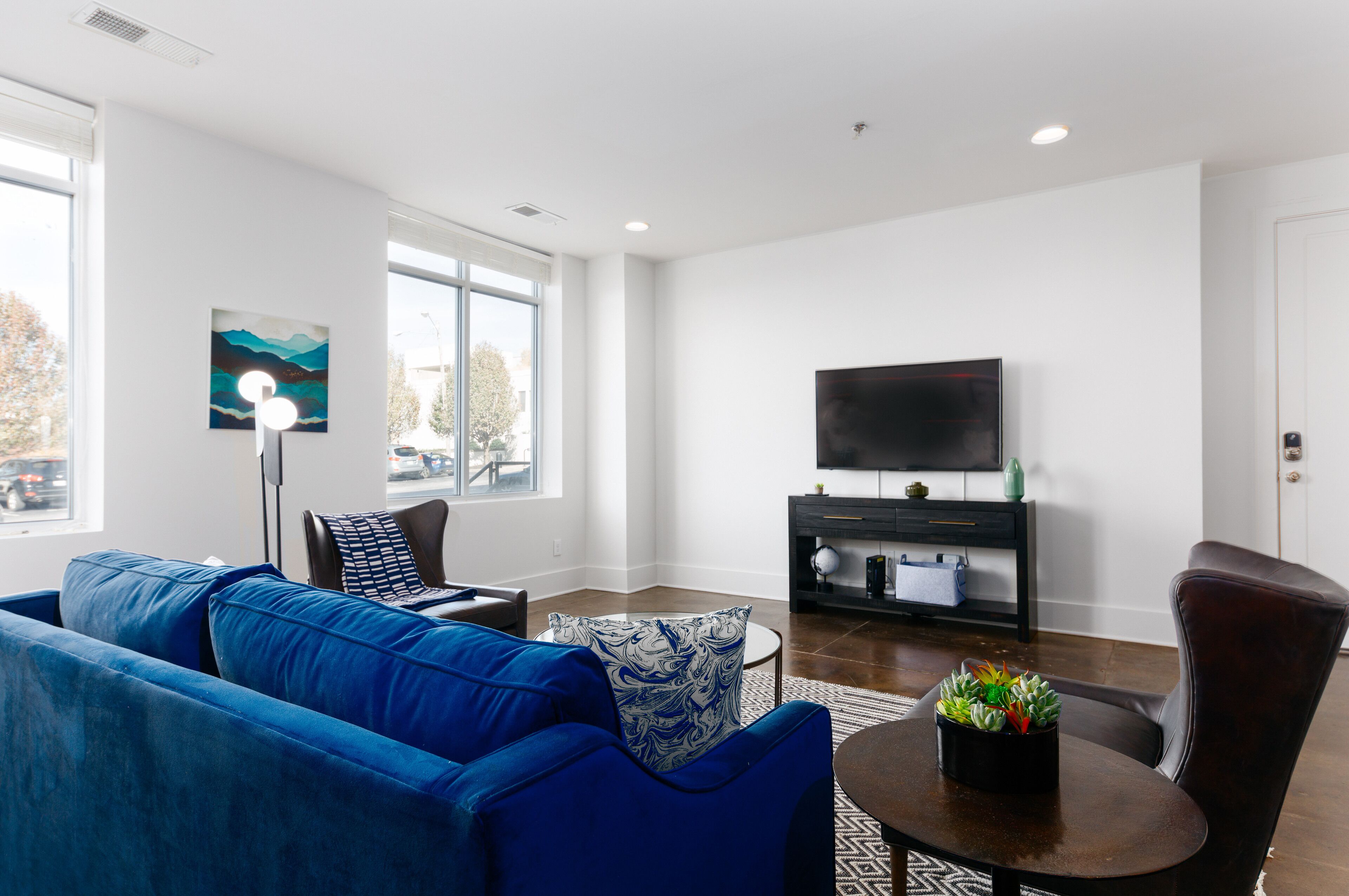 A modern living room with a blue sofa, a round coffee table, a flat-screen TV, and a large window.