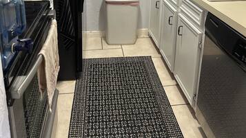 A compact kitchen with a refrigerator, a coffee maker, a trash bin, and a sink.