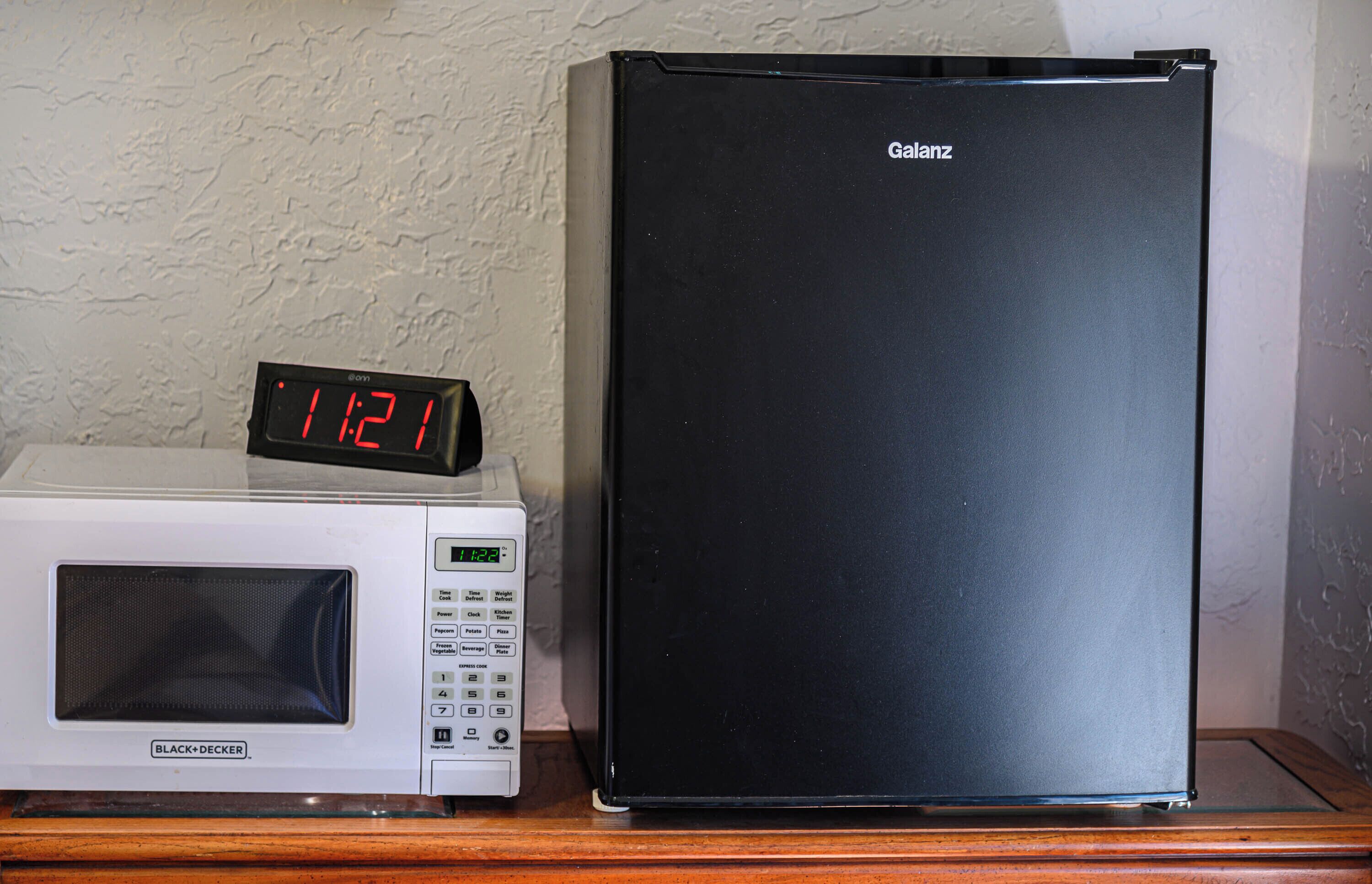 Un microondas y un refrigerador negro sobre una superficie de madera frente a una pared con textura.
