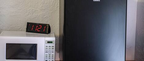 Un microondas y un refrigerador negro sobre una superficie de madera frente a una pared con textura.