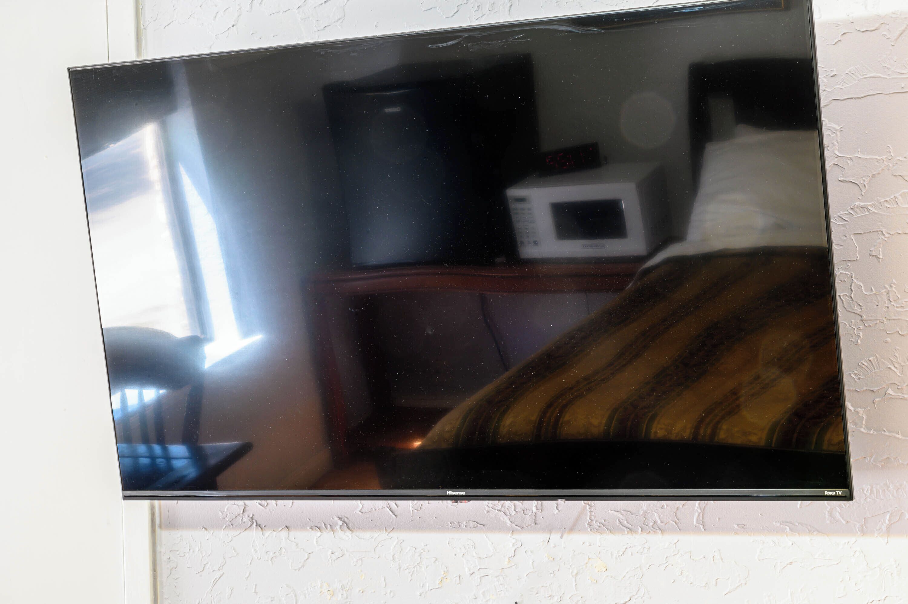 Un televisor montado en la pared, un microondas y una cama con una colcha a rayas.