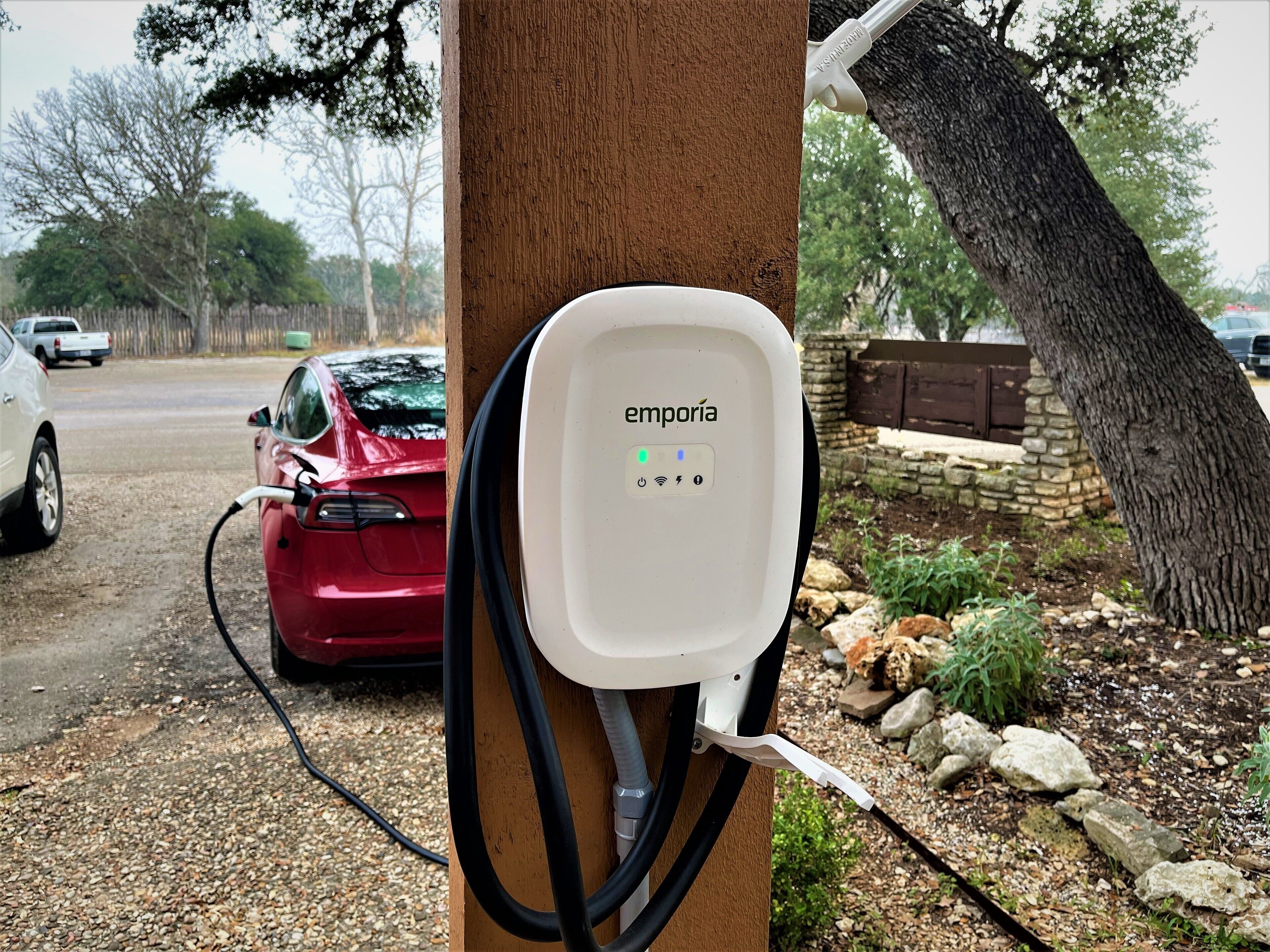 Une borne de recharge pour véhicules électriques, dotée d’une boîte blanche portant l’inscription « emporia » et fixée sur un poteau en bois.