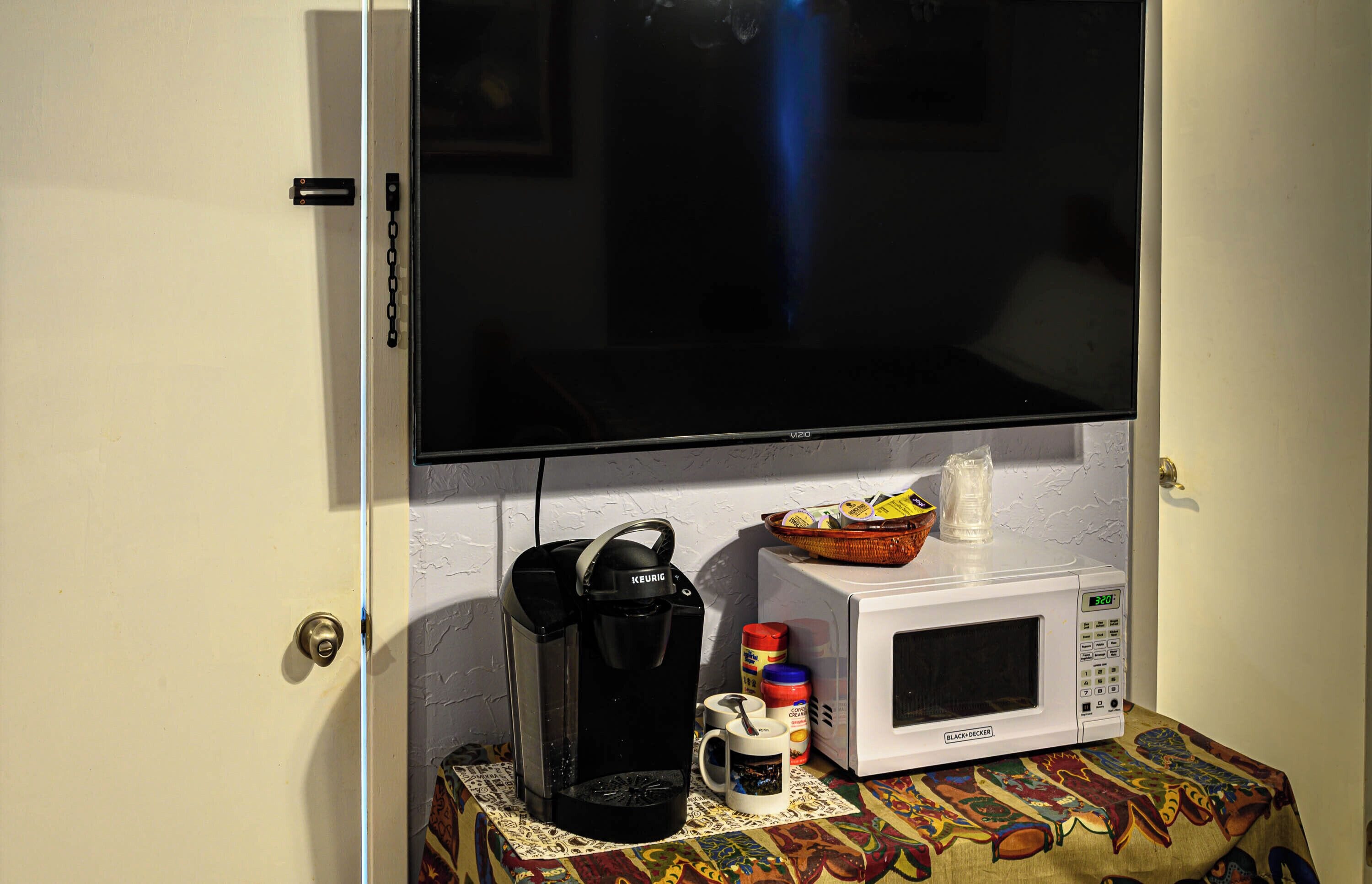 A kitchenette with a coffee maker, microwave, and a small table with a patterned tablecloth.