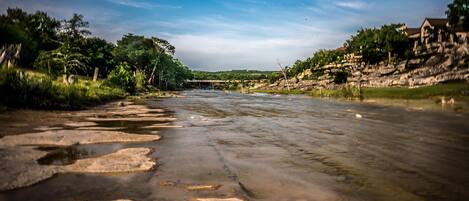 A river with clear water, surrounded by greenery and a bridge in the distance.
