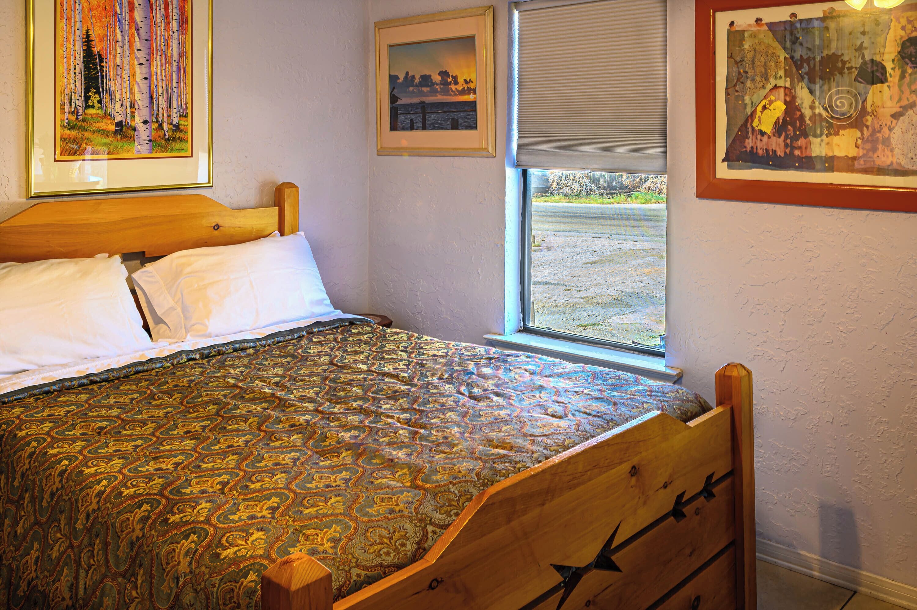 A bedroom with a wooden bed, a patterned bedspread, and three framed pictures on the wall.