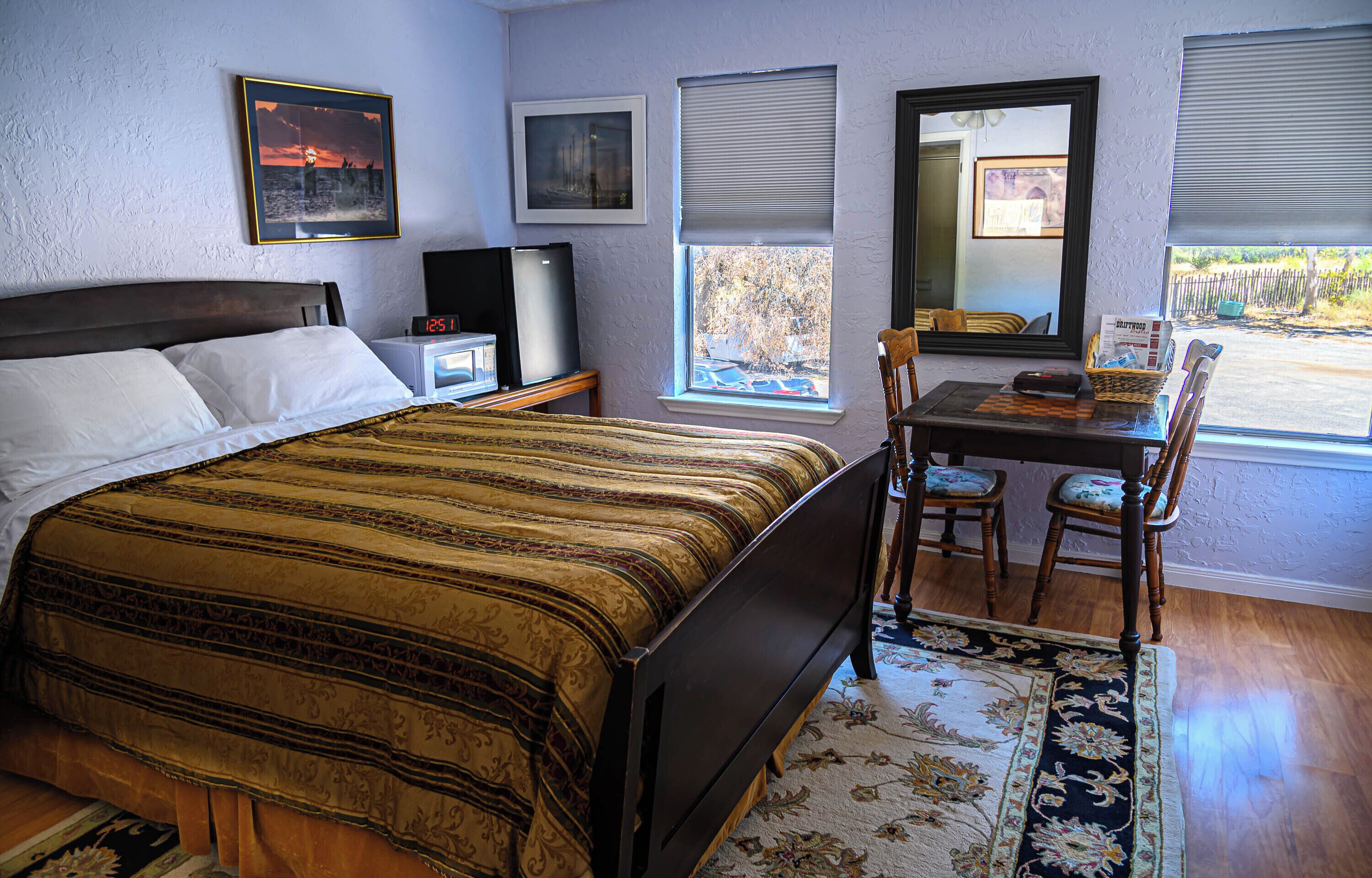 A bedroom with a bed, a desk, two chairs, a TV, and a window with blinds.