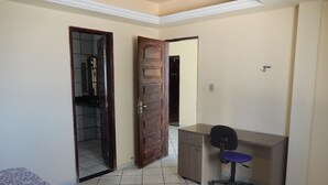 Une chambre avec un lit, un bureau et une chaise. Il y a deux portes, l’une donnant sur une salle de bain et l’autre sur un placard.