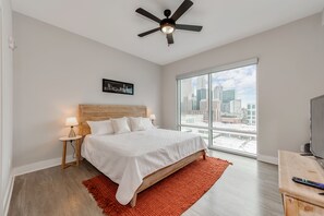Ein modernes Schlafzimmer mit einem großen Bett, Blick auf die Stadt, Deckenventilator und einem Fernseher auf einem Holzboden.