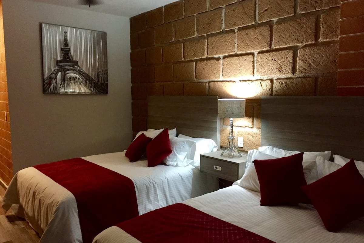 A hotel room with two beds, a brick wall, a lamp, and a painting of the Eiffel Tower.