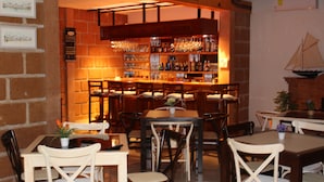 A bar area with wooden furniture and a brick wall. There are multiple tables and chairs, and a variety of bottles and glasses on shelves. - Hotel Boutique La Herencia (Tequisquiapan)