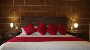 A hotel room with a brick wall, a large bed with white bedding and red pillows, and two bedside lamps. - Hotel Boutique La Herencia (Tequisquiapan)