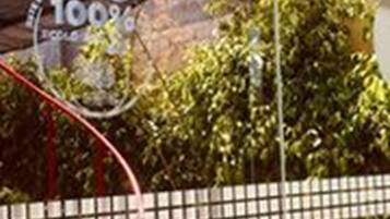 A basketball hoop with a logo, a fence, and greenery in the background.