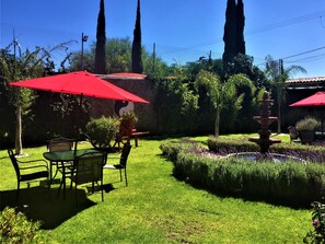 Un jardin bien entretenu, agrémenté d’une fontaine, de parasols rouges et de haies soigneusement taillées.