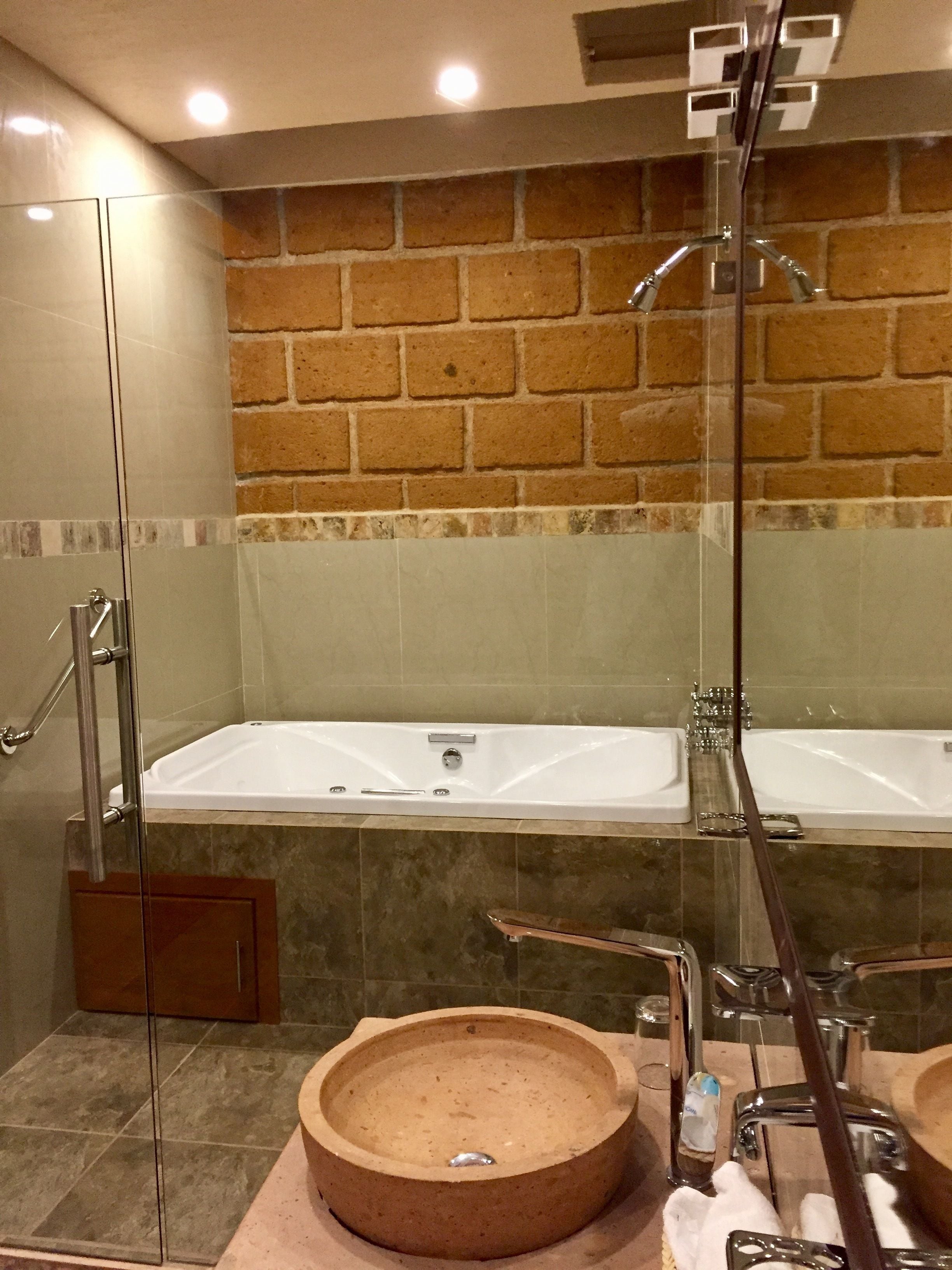 A bathroom with a glass-enclosed shower, a large bathtub, and a round sink.