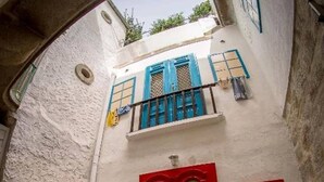 Un bâtiment blanc avec une porte rouge, des volets bleus et un petit balcon.