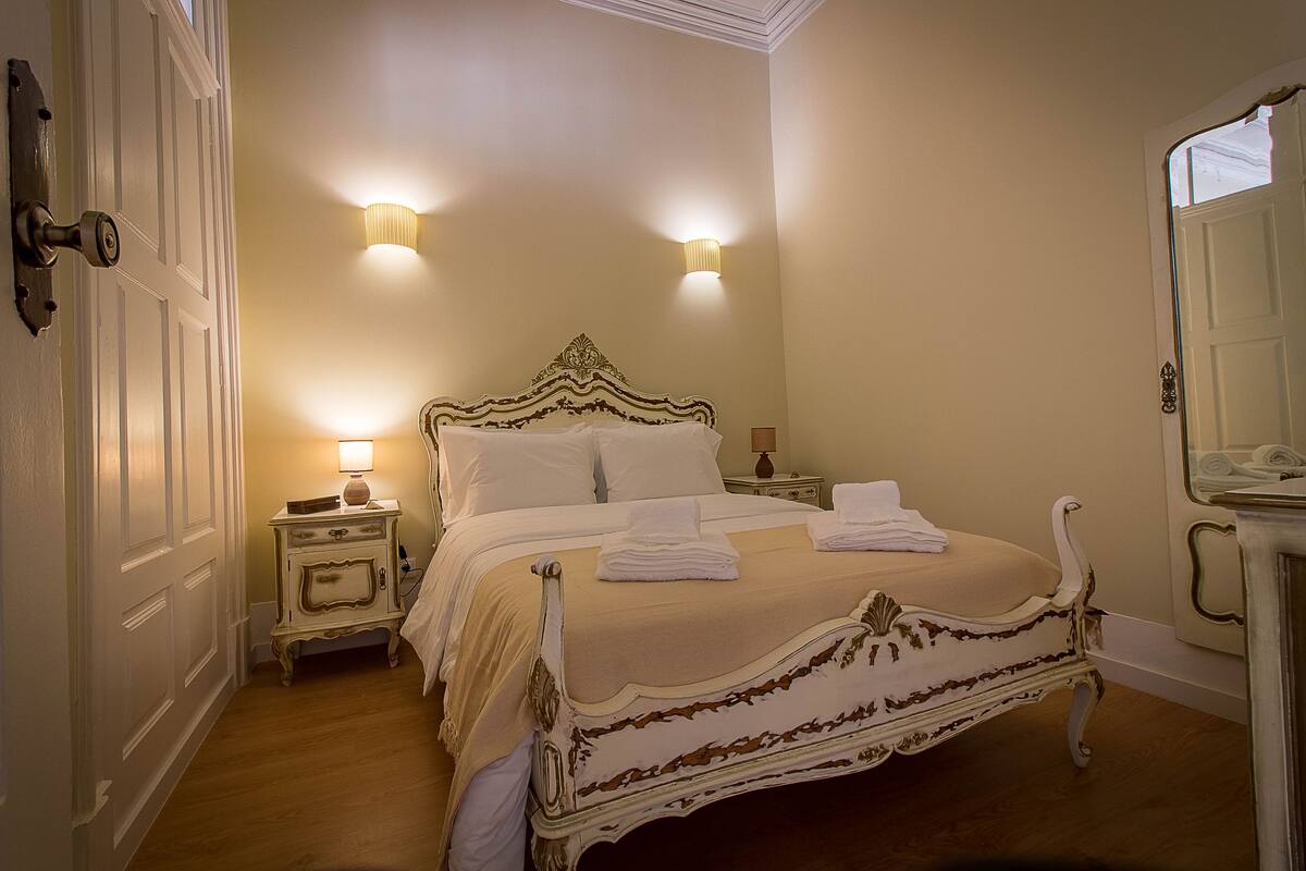 A bedroom with a four-poster bed, two bedside lamps, and a nightstand with a lamp.