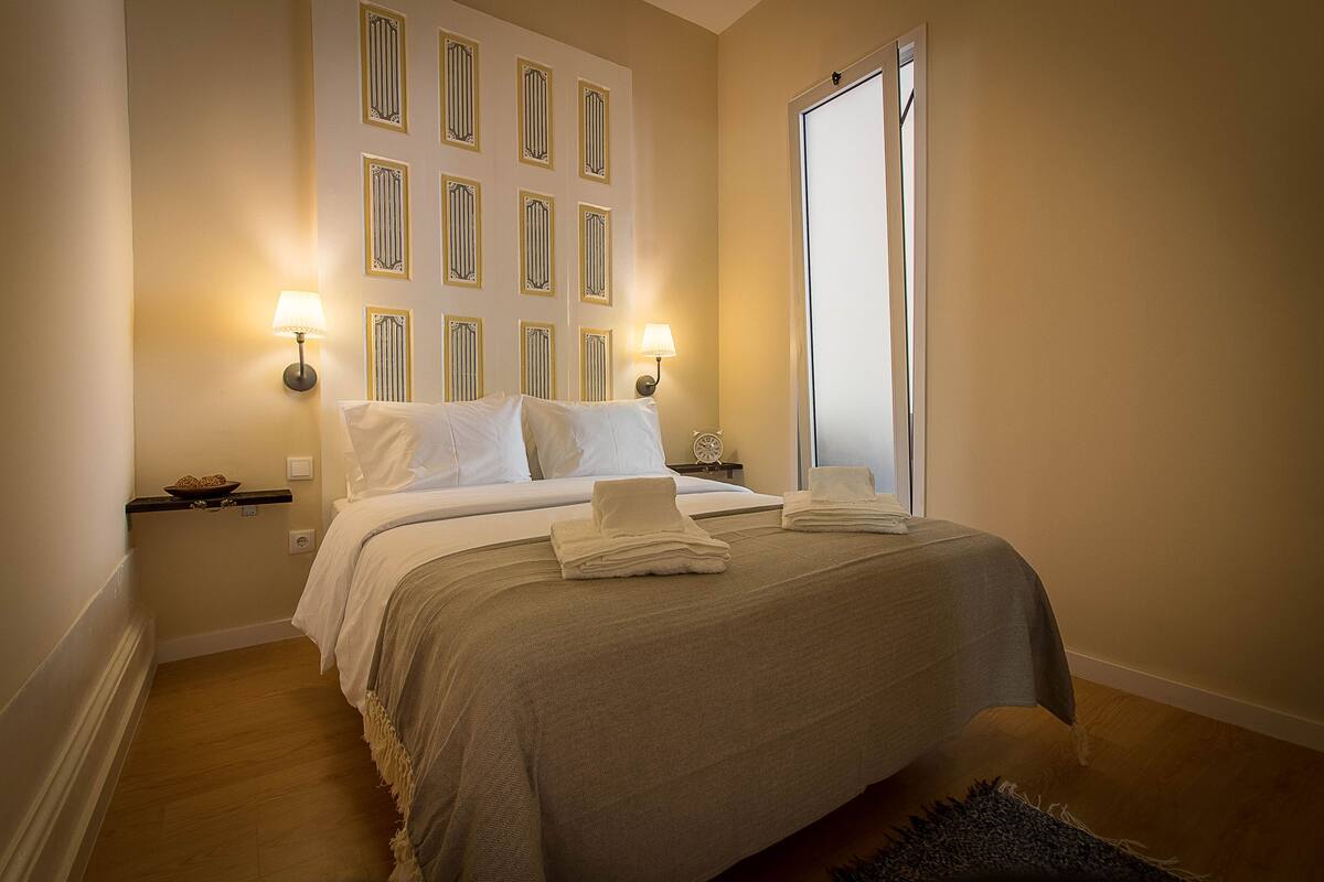 A neatly made bed with a beige bedspread, two bedside lamps, and a wall with decorative panels.