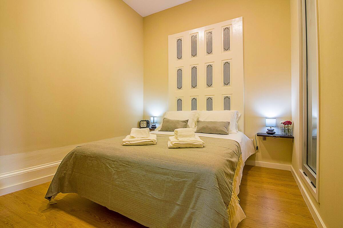 A neatly made bed with towels, a bedside table with a lamp, and a window with a view.