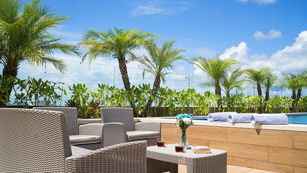 A rooftop lounge with wicker furniture, a pool, and tropical plants. - Opal Apt. 402 Better in Person Than in the Pictures (Playa del Carmen)