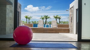 A modern room with a large exercise ball, a view of a pool area with lounge chairs, and a wooden deck. - Opal Apt. 402 Better in Person Than in the Pictures (Playa del Carmen)
