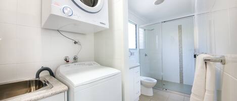 A modern bathroom with a washing machine, a sink, a toilet, and a glass-enclosed shower area.