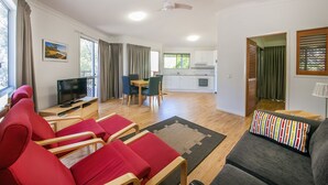 Una sala de estar moderna con un sofá gris, sillas rojas, un televisor y un comedor con una mesa y sillas.